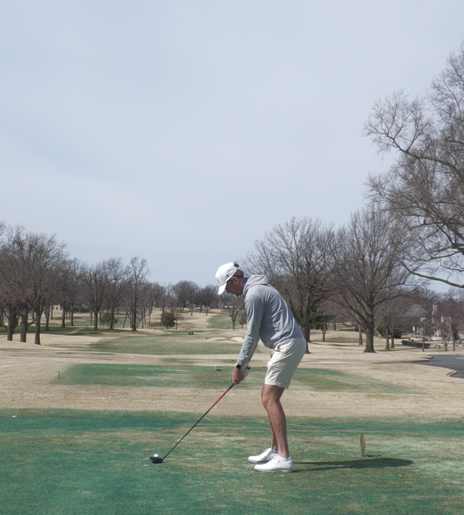 golf fitting tulsa - Tour Quality Golf | Indoor Lessons, Fittings & Virtual Golf A golfer in a gray hoodie and white cap tees off from a grassy practice area on a sunny course.