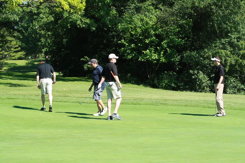 fitting-golf-club - Tour Quality Golf | Indoor Lessons, Fittings & Virtual Golf Four golfers walk and stand on a sunny golf green with trees in the background a short distance away from the hole.